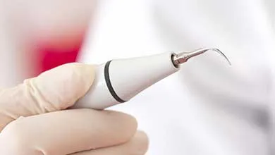 Gloved hand holding a dental scaler with a curved metal tip.